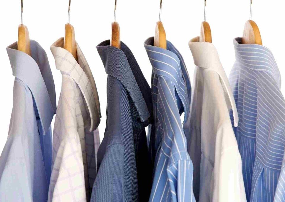 Men's dress shirts hanging on wooden hangers.