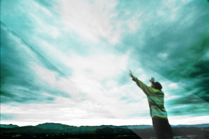 Person reaching towards cloudy sky, vibrant colors.