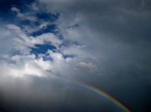 Rainbow beneath cloudy sky after rain.