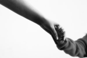 Adult and child holding hands in grayscale.