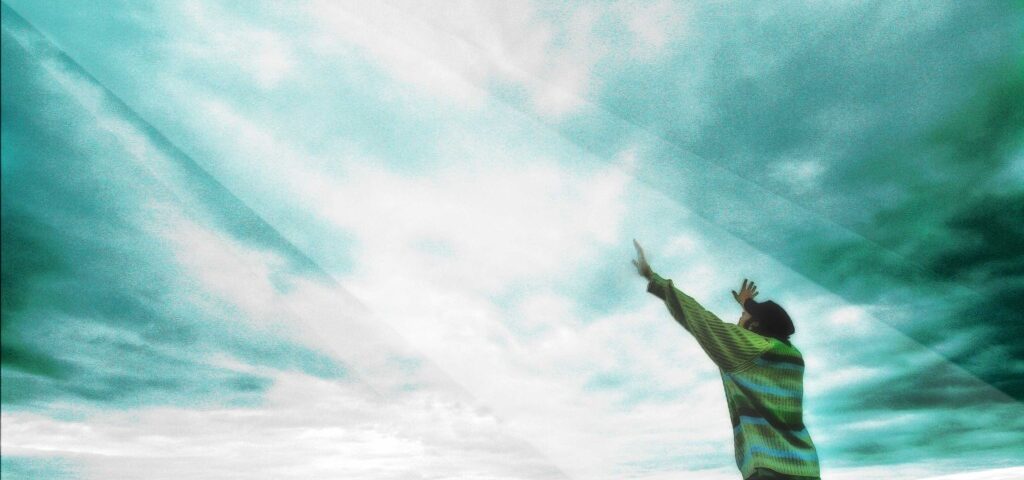 Person reaching towards cloudy sky, mountainous background.