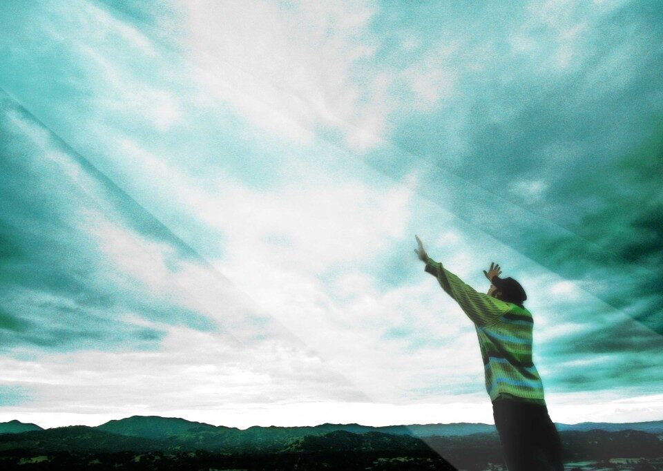 Person reaching towards a cloudy sky.