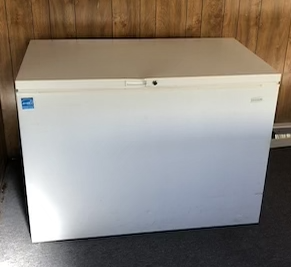 White chest freezer with a lock on top in a wooden room.