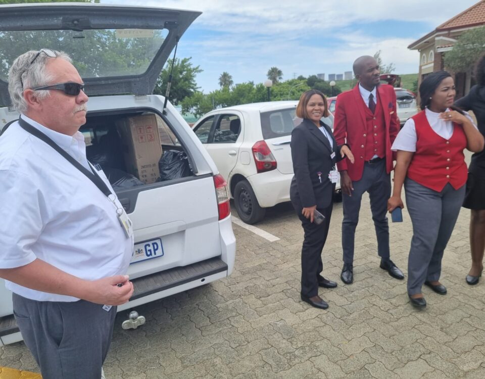 A group of four people standing near parked cars outdoors on a sunny day.