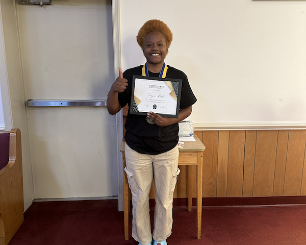 Person proudly holding a certificate and giving a thumbs up indoors.