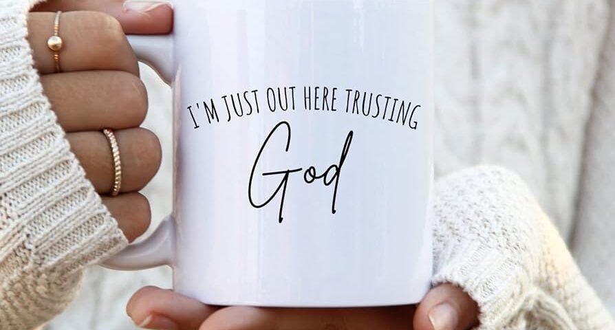 White mug with the phrase 'I'm just out here trusting God'.