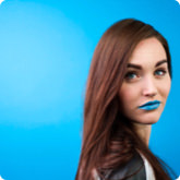 Woman with brown hair and blue lipstick against a blue background.